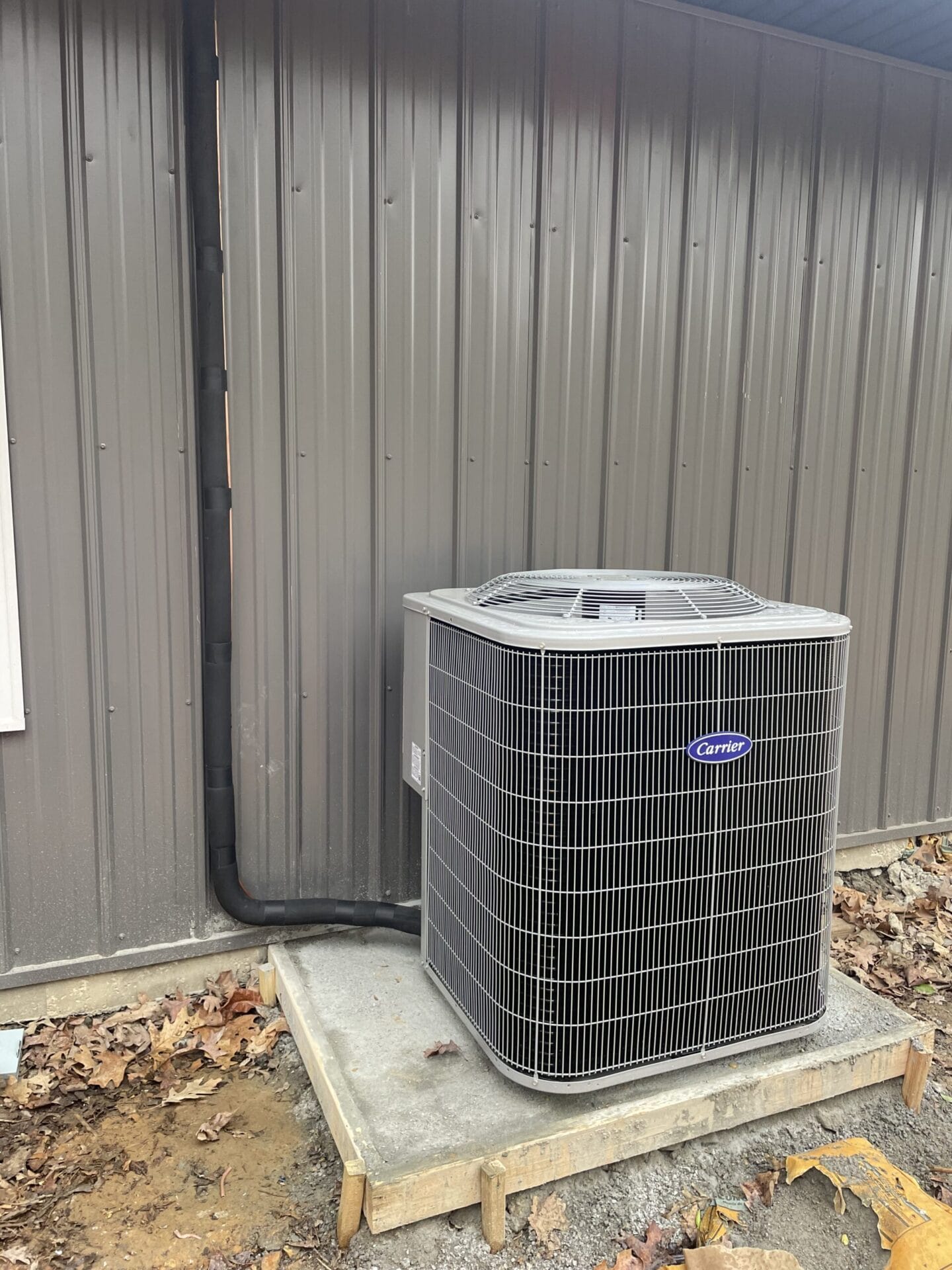 Outdoor HVAC unit on a concrete pad next to a metal building with fallen leaves on the ground.