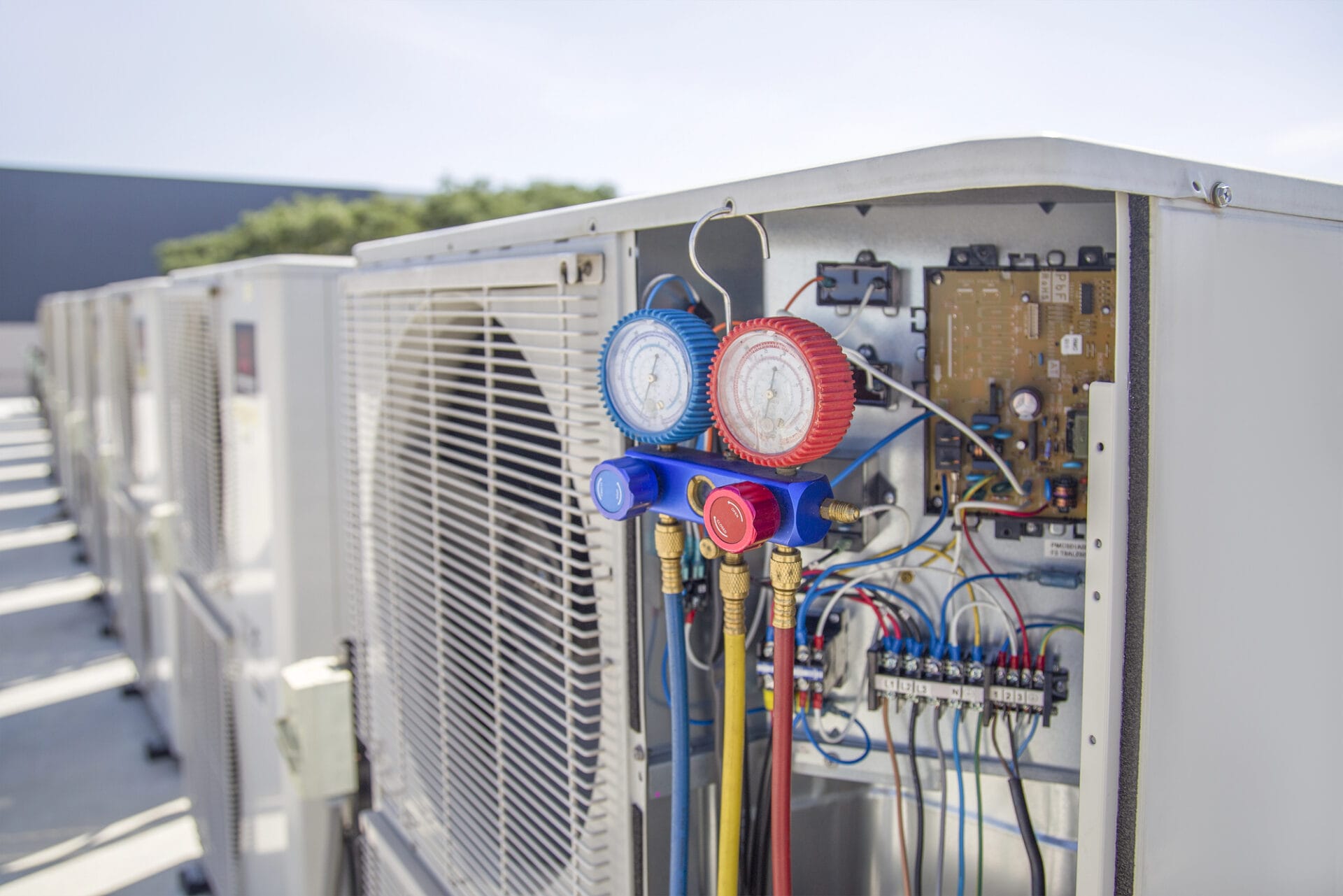 A row of industrial air conditioning units with one panel open, revealing circuitry and attached pressure gauges.