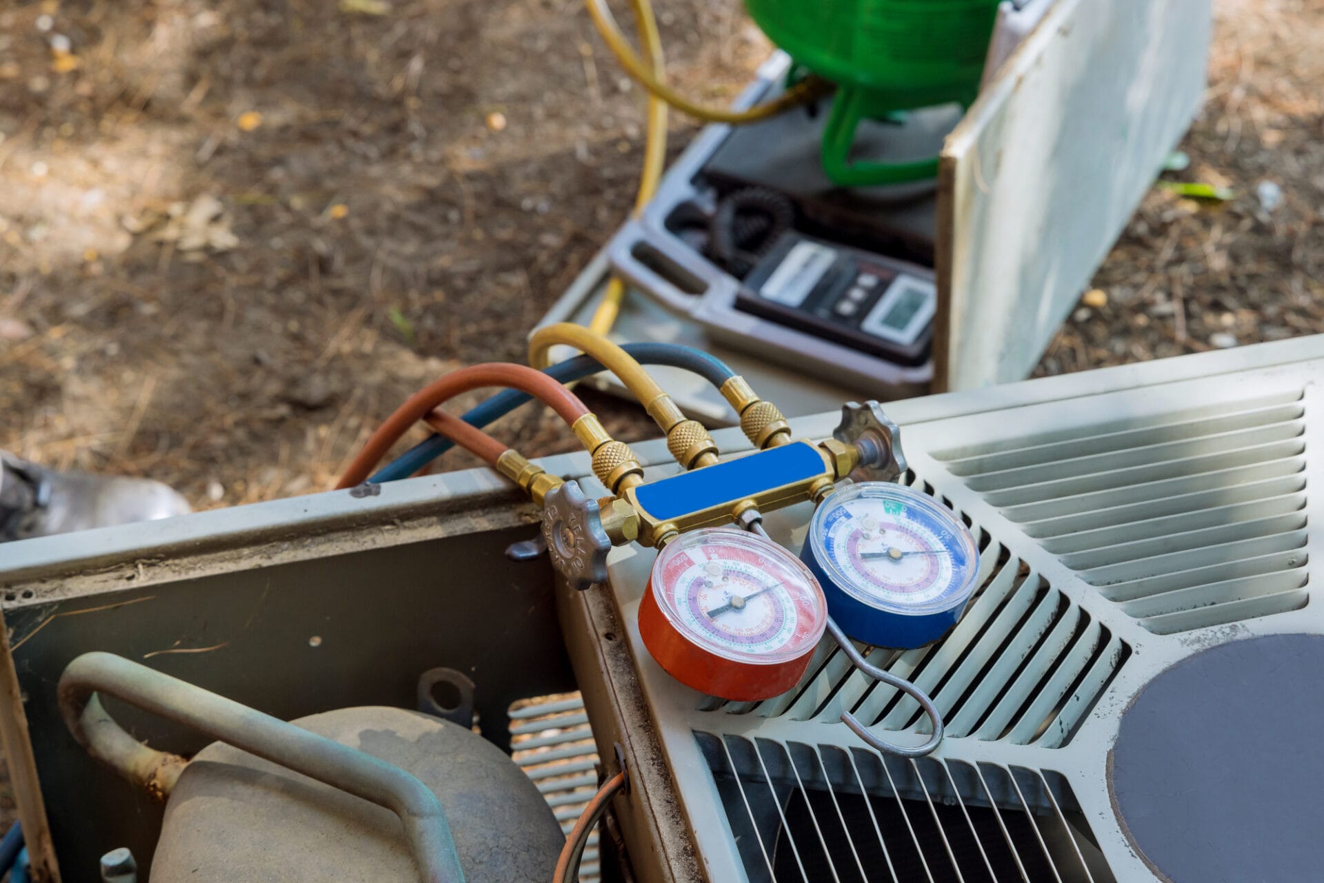 HVAC manifold gauges connected to an air conditioning unit, with pressure readings visible.