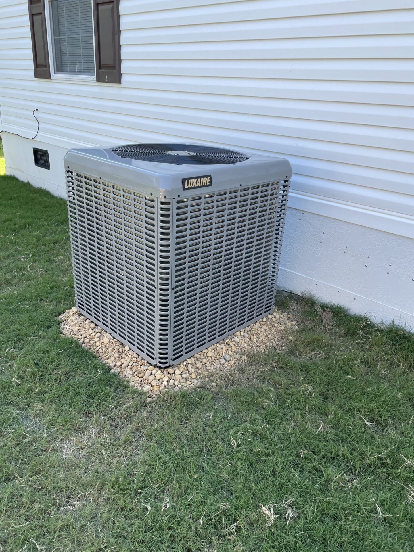 Outdoor air conditioning unit on a gravel base next to a white building.