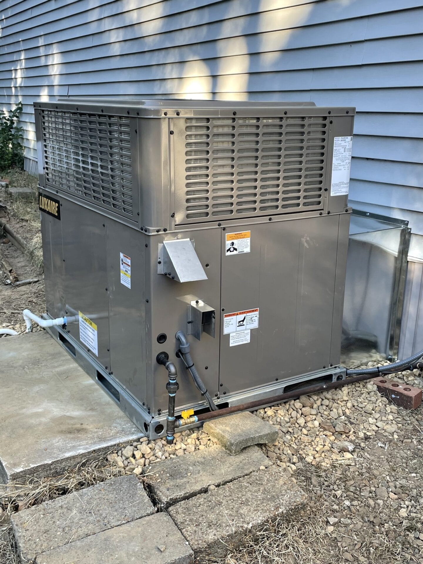 Large outdoor HVAC unit next to a building, on a concrete pad surrounded by gravel and dirt.